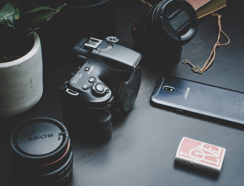 A modern camera setup featuring lenses, a smartphone, and a lighter arranged on a desk.